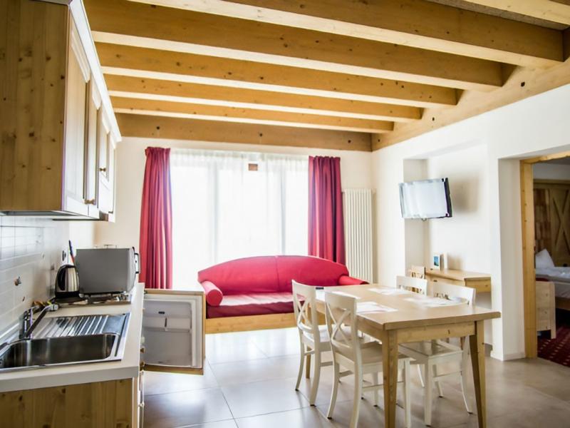 Accogliente soggiorno con cucina in legno, divano rosso e luce calda.