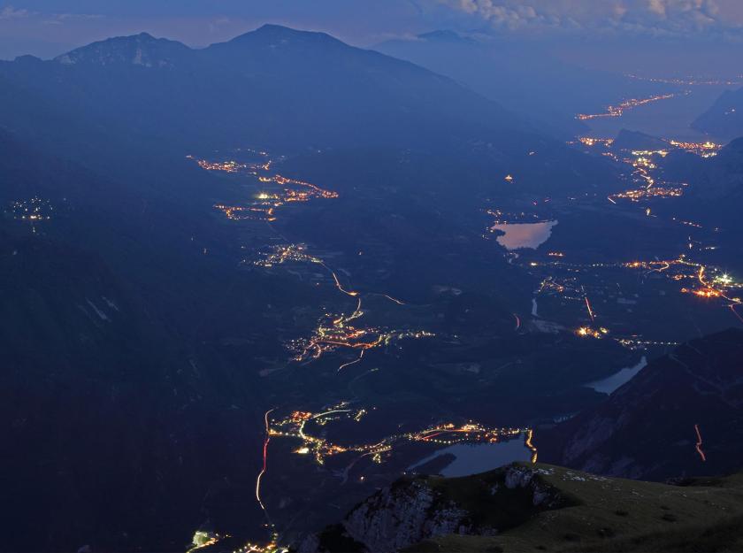 Vista notturna di una valle illuminata con laghi e montagne sullo sfondo.